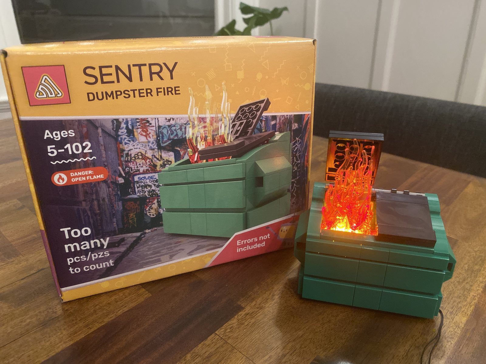 A boxed Sentry Dumpster Fire toy beside a small green dumpster holding an orange flame.